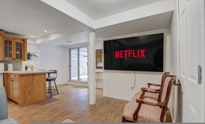 Una cocina moderna con armarios de madera, un comedor con barra y un televisor de pantalla plana grande mostrando el logo de Netflix.