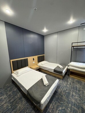 A hotel room with two single beds, a bunk bed, and a small bedside table.