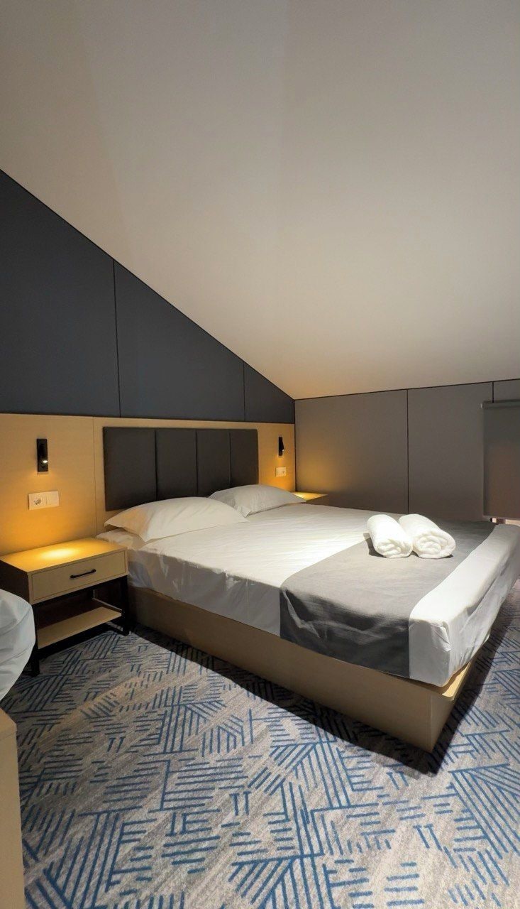 Ein modernes Hotelzimmer mit einem großen Bett, Nachttischen und einem gemusterten Teppich.
