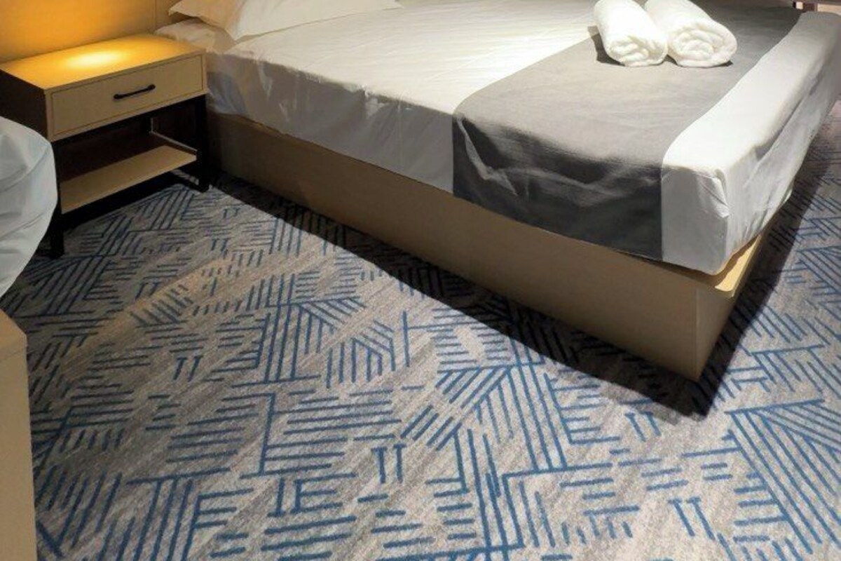 A modern hotel room with a large bed, bedside tables, and a patterned carpet.