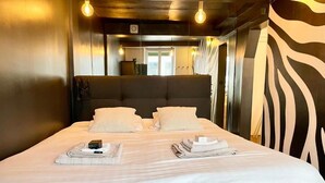 Une chambre d’hôtel avec un grand lit, deux oreillers, une table de chevet avec une lampe et un mur orné d’un motif zébré.