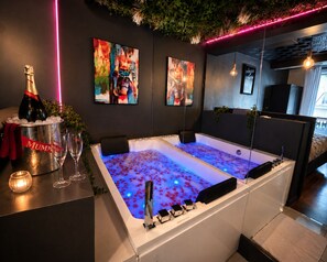 A modern bathroom with a large bathtub, a champagne bottle, and glasses on a counter. - Champs‑Elysées Loveroom & Spa (Paris)