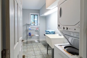Ein kleiner Waschraum mit Waschmaschine, Waschbecken und Regalen voller Reinigungsmittel.