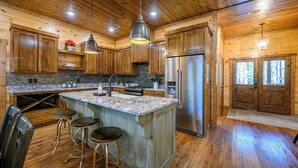 A kitchen with wooden cabinets, a granite countertop, stainless steel appliances, and a bar area with stools. - Near Broken Bow Lake • Games, Hot Tub & Fun for All Ages (broken bow)