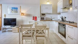A modern kitchen with white cabinetry, a dining area with white chairs, a flat-screen TV, a microwave, and a stove.