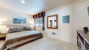 Un dormitorio con una cama grande, una mesita de noche con lámpara, un aparador, un espejo y dos cuadros en la pared.