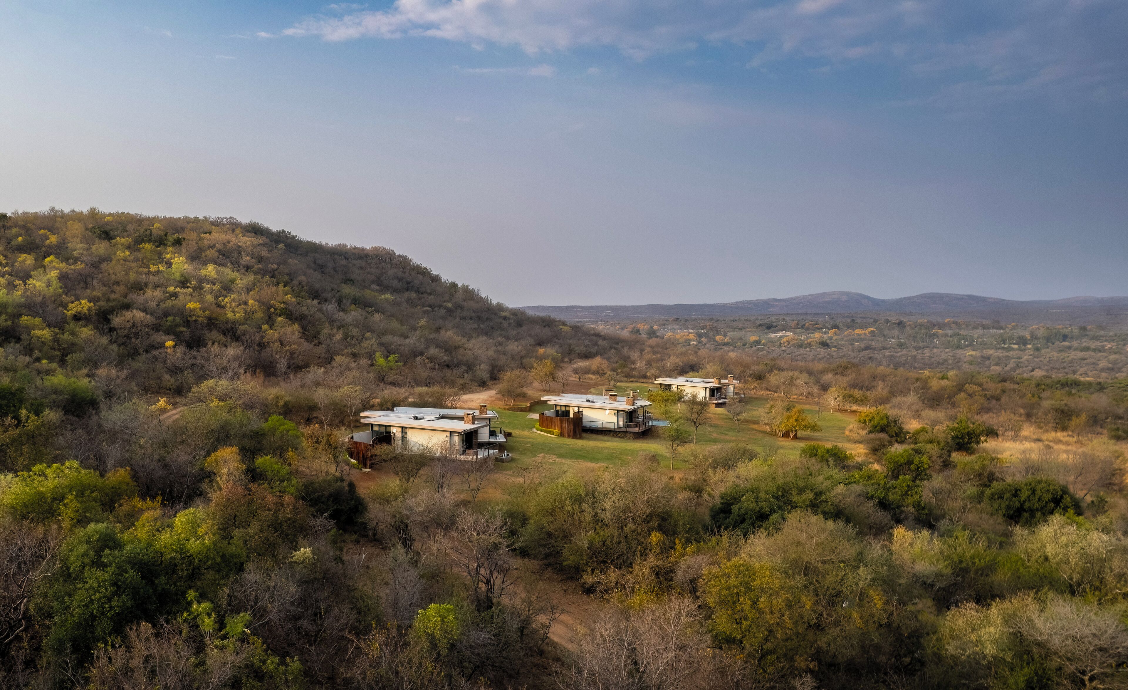 A remote, modern resort with three contemporary buildings nestled in a hilly, forested landscape.