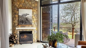 A living room with a stone fireplace, a glass coffee table, and a view of the outdoors. - Babirwa Game Ranch (Rooiberg)