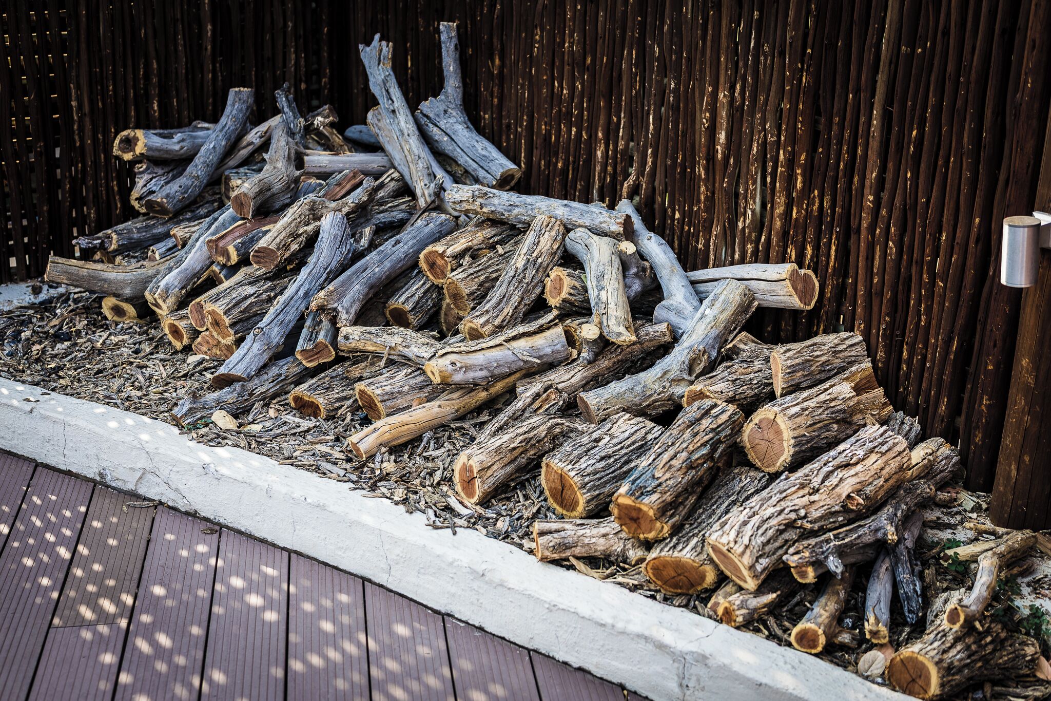 Une pile de bûches empilées contre une clôture en bois.