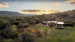 A modern house with a flat roof, surrounded by a grassy area and dense shrubbery. - Babirwa Game Ranch (Rooiberg)