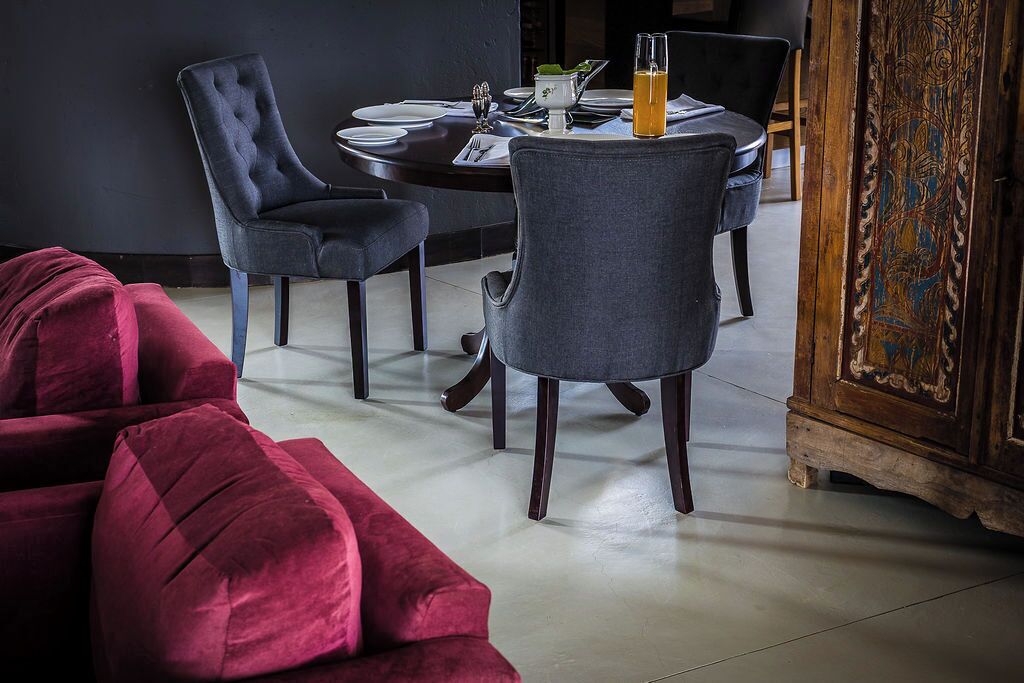Un'area pranzo con un tavolo rotondo apparecchiato per due persone, due poltrone imbottite, un divano rosso e un mobile in legno con intagli elaborati.