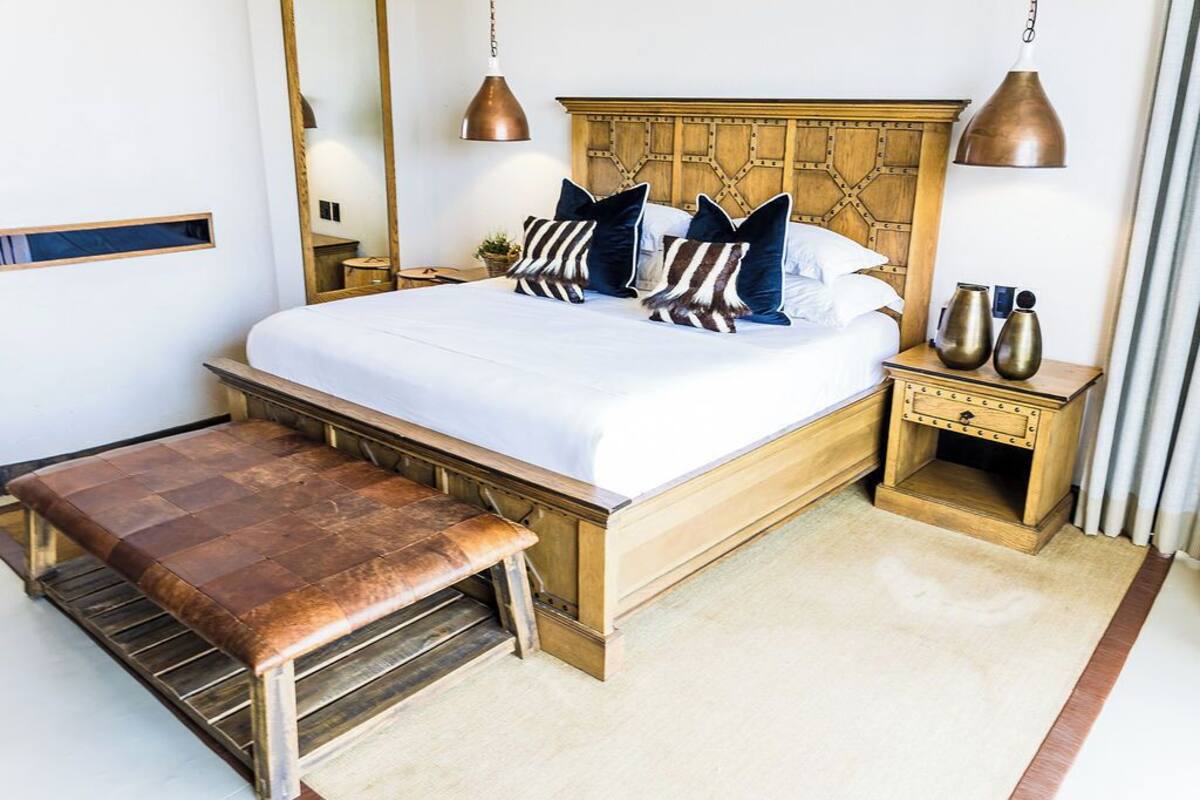 A neatly arranged bedroom with a wooden bed, matching nightstands, a bench, and a mirror on the wall.
