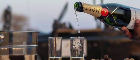A bottle of Moët & Chandon champagne being poured into two glasses, with a wooden board of cheeses and crackers in the background.