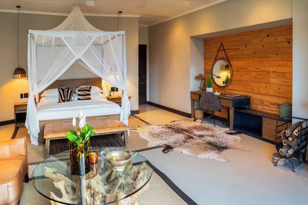 A modern bedroom with a canopy bed, a desk, a mirror, and a leather rug.