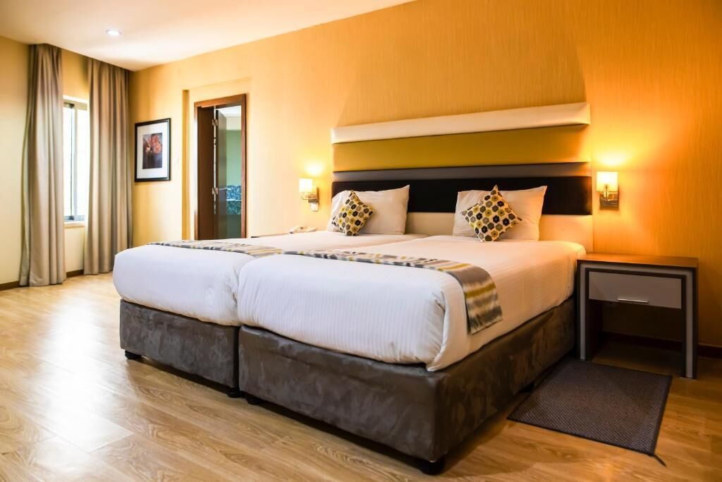 Una cama doble con cabecera, mesitas de noche y una ventana con cortinas.