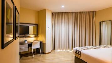 Quarto de hotel com cama, escrivaninha, cadeira e uma grande janela com cortinas.