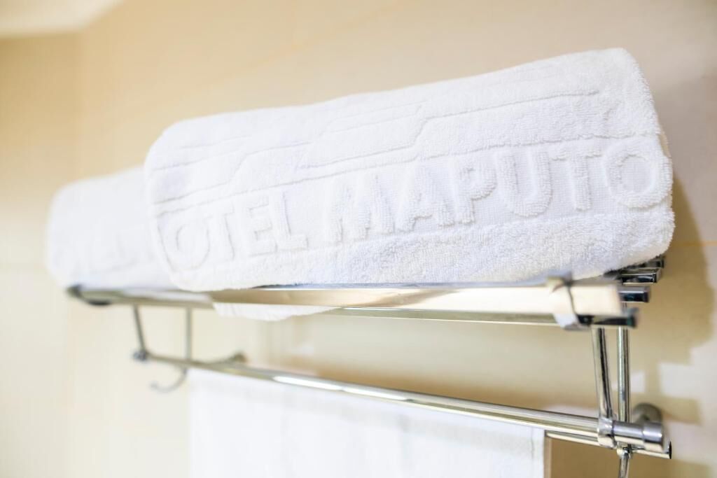 A white towel with 'HOTEL MAPUTO' embossed on it, hanging on a metal towel rack.
