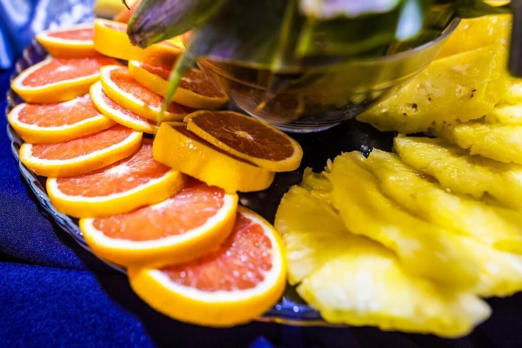 A plate with sliced oranges and pineapple arranged on a blue cloth.