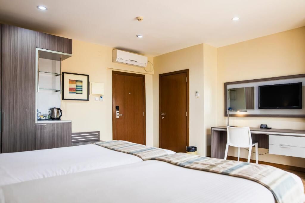 A hotel room with a bed, a desk with a chair, a television, and an air conditioning unit.