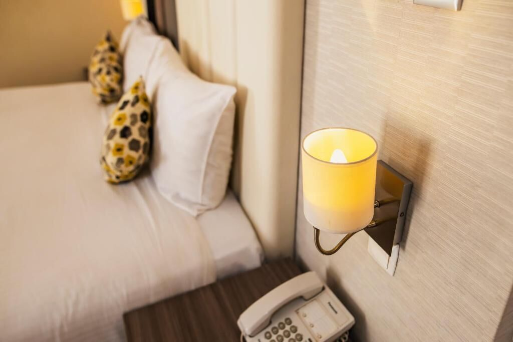 Habitación de hotel con cama, lámpara de noche, teléfono y almohadas de estampado de leopardo.