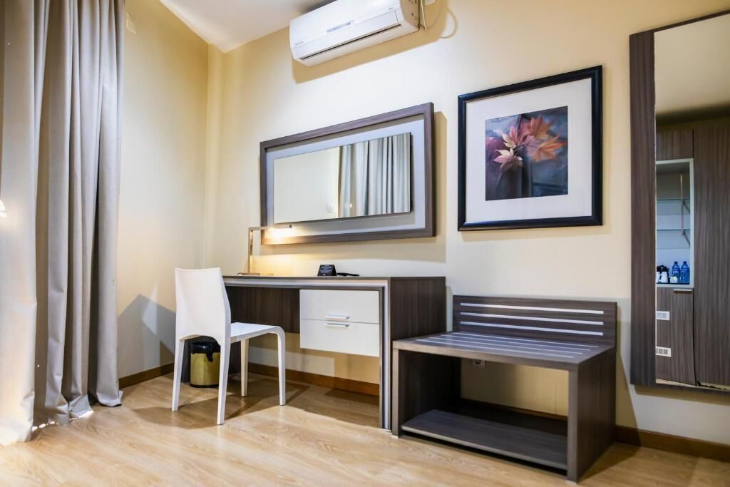 A hotel room with a desk, chair, bedside table, and a large mirror.