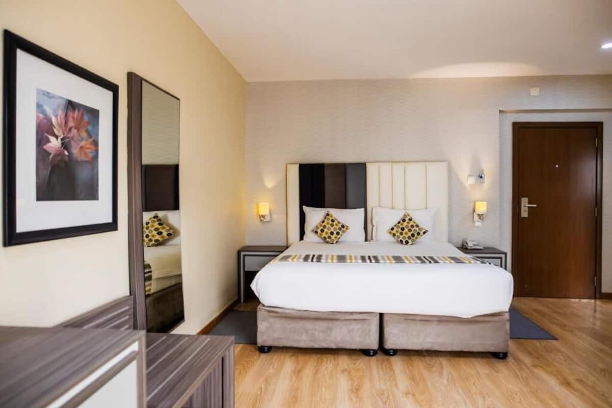 A hotel room with a large bed, bedside tables, a mirror, and a framed picture on the wall.