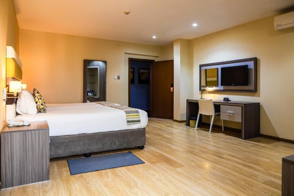 A hotel room with a bed, desk, chair, TV, and a mirror.