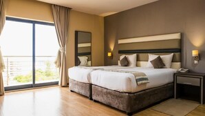 A double bed with a headboard, a bedside table with a lamp, and a large window with curtains. - WL Hotel Maputo City Center (Maputo)