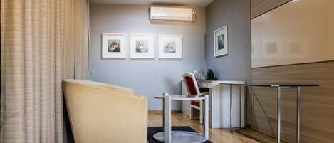 Una habitación de hotel moderna con sofá, un escritorio pequeño, una silla y cuadros en la pared.
