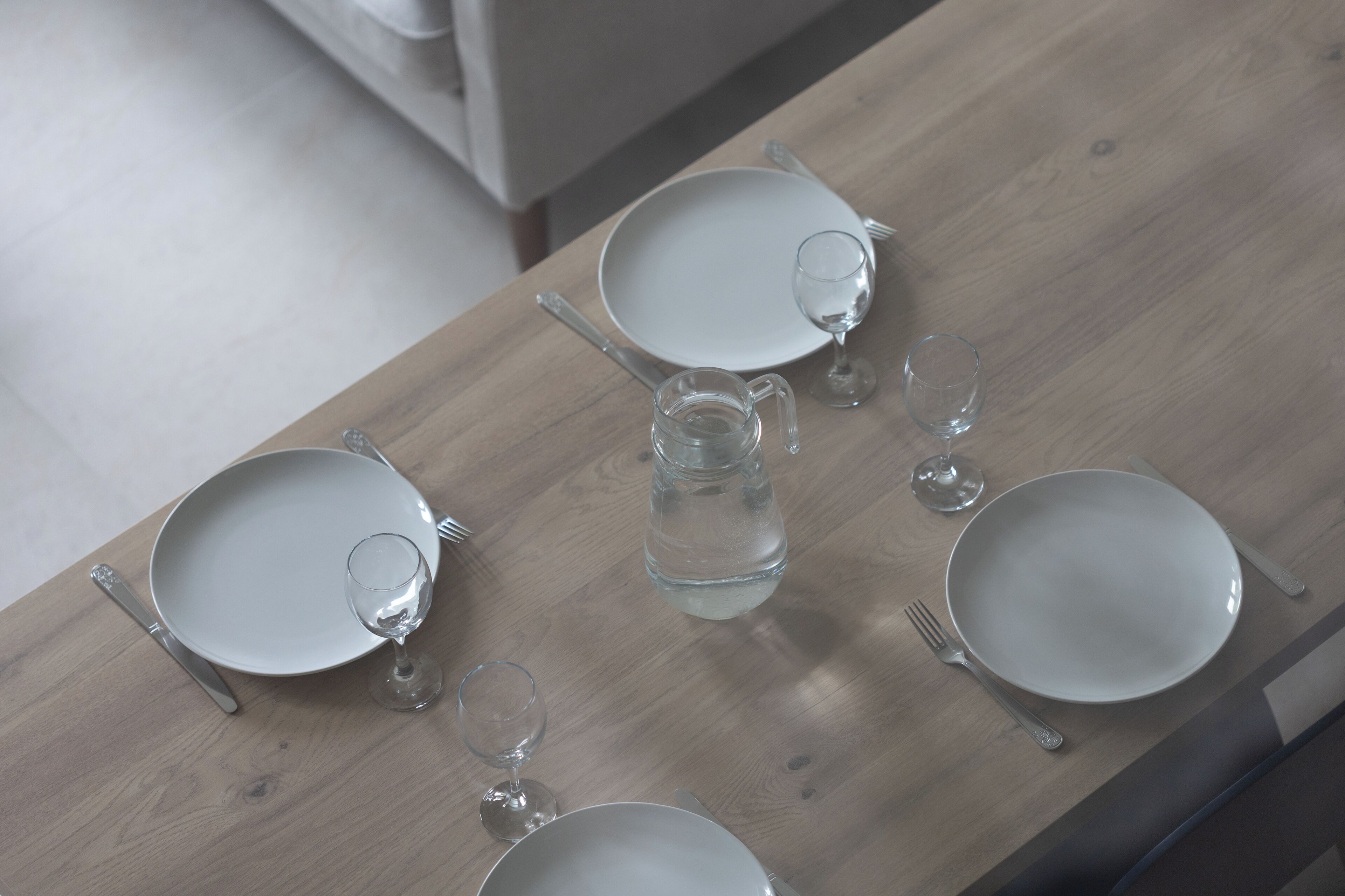 A dining table with four plates, cutlery, and glasses, set on a wooden surface.