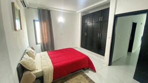 A bedroom with a bed, a wardrobe, a mirror, and a door. - Elegant 2-bedroom Apartment in Chic Abidjan Neighborhood (Abidjan)