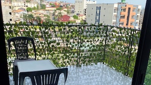 A balcony with a table and chairs, a metal fence, and a view of buildings in the distance. - Elegant 2-bedroom Apartment in Chic Abidjan Neighborhood (Abidjan)