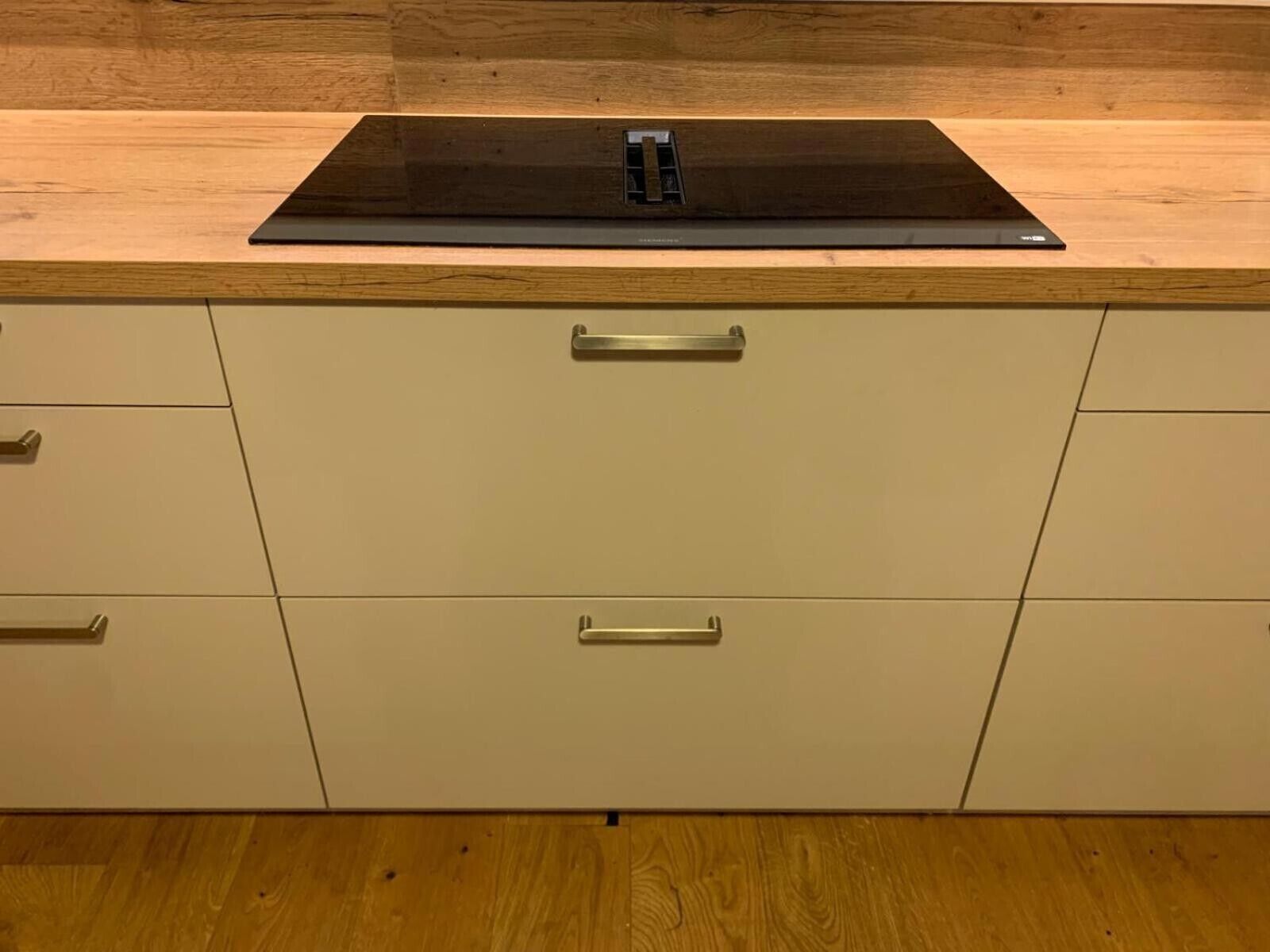 Una cocina con encimera negra, armarios blancos y suelo de madera.