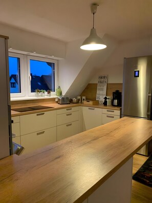 A modern kitchen with a wooden countertop, white cabinets, a stainless steel refrigerator, and a window with a view of houses. - Apartment near Clemens Hospital with Balcony and Wi-Fi (Münster)