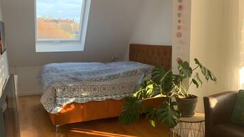 Un dormitorio con cama, ventana, planta en maceta, sofá y una mesita.