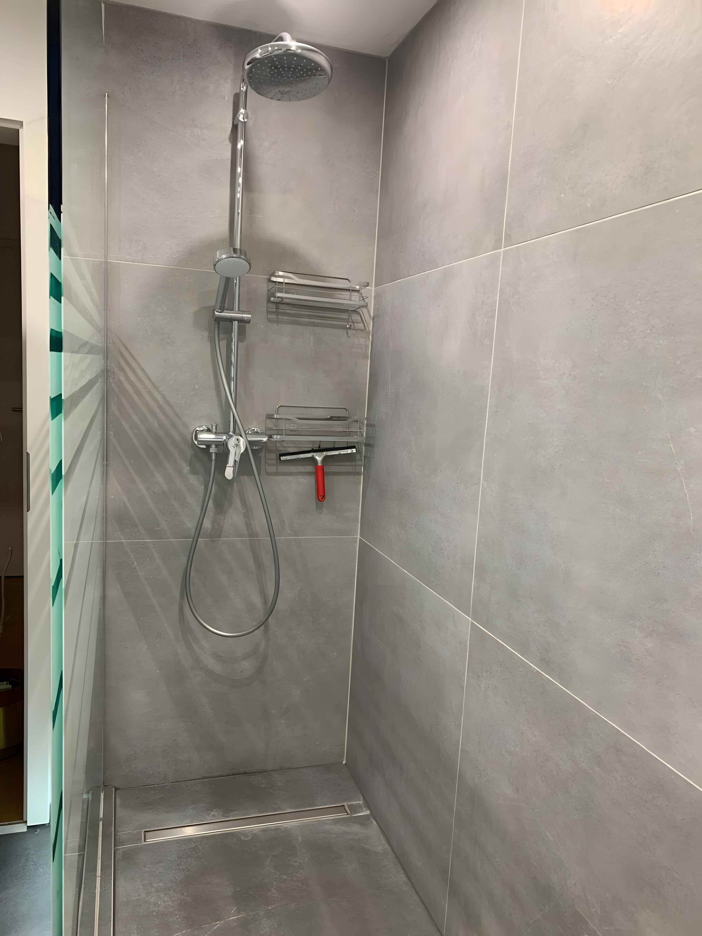 En dusch med ett duschhuvud som kan hållas i handen, en väggmonterad blandare och ett rött duschhuvud som kan hållas i handen.