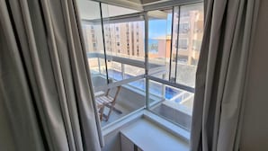 Een kamer met een groot raam dat uitkijkt op een balkon met een houten stoel.