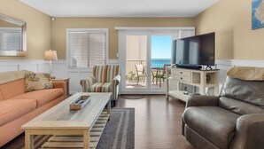 A living room with a sofa, armchair, TV, and a balcony with a view.
