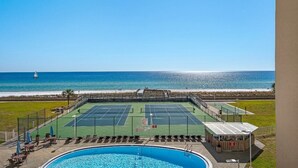 A tennis court with a pool and beach view.