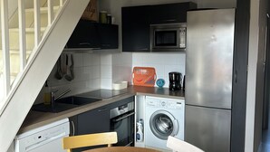 A modern kitchen with a dining area, including a wooden table, chairs, a washing machine, a refrigerator, and a microwave. - Apartment in Les Hameaux de l'océan 200m from the ocean (Carcans)