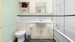A bathroom with a white sink, toilet, and shower. There are cabinets above the sink and a mirror above it. - 2bed 2bath close to Tower Bridge (London)