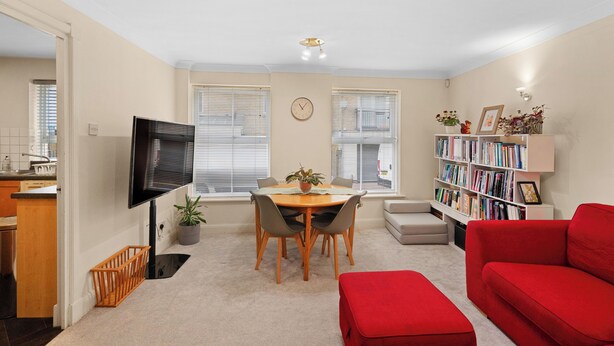 A living room with a red couch, a dining table with chairs, a bookshelf, and a TV mounted on the wall. - 2bed 2bath close to Tower Bridge (London)