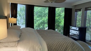 Habitación de hotel con cama, ventilador de techo y ventanas grandes con cortinas.