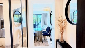 Un interior moderno con un separador de vidrio, una zona de comedor con una mesa redonda y sillas, y un espejo grande en la pared.