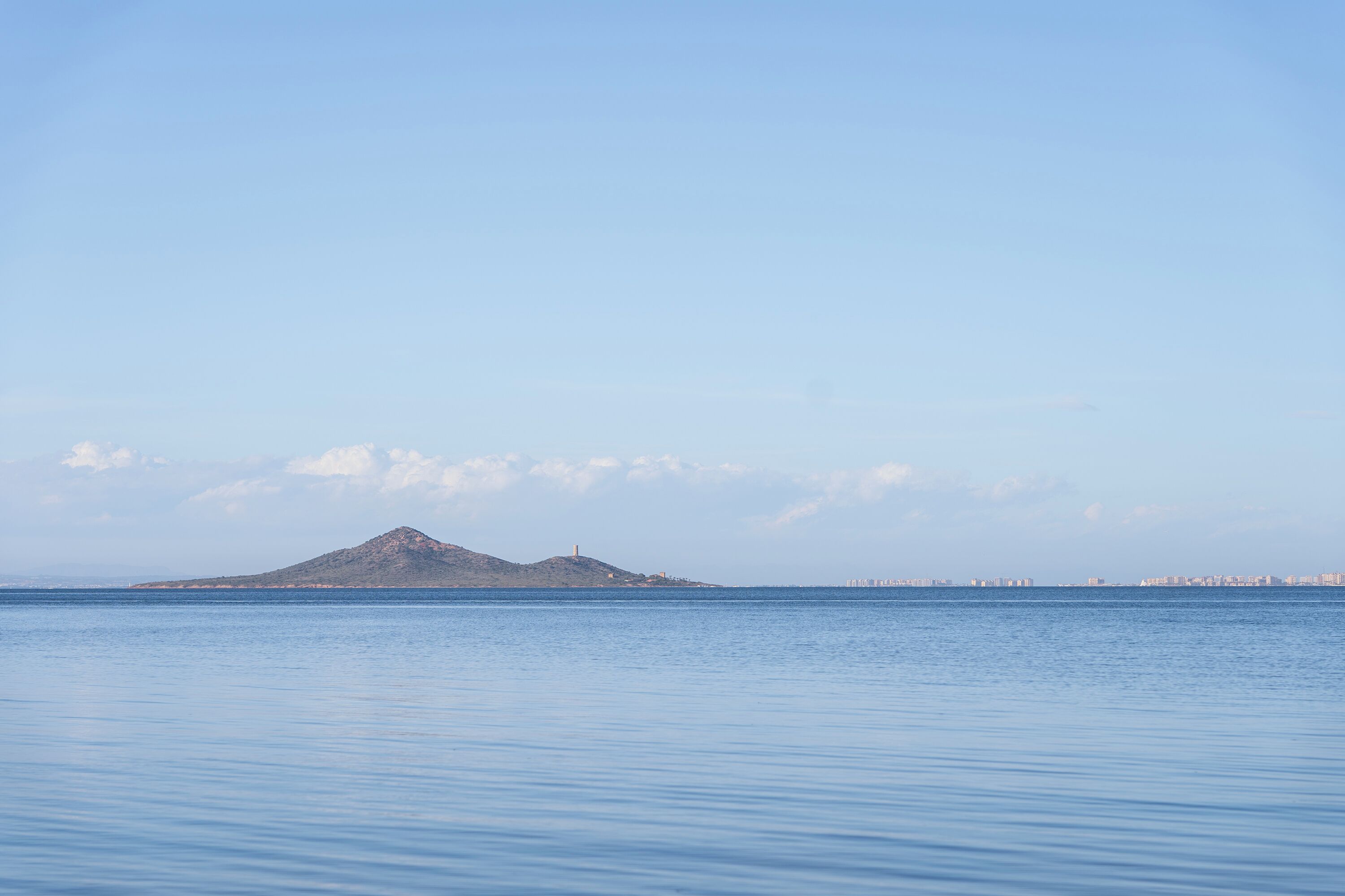 A calm sea with a distant island and a lighthouse.