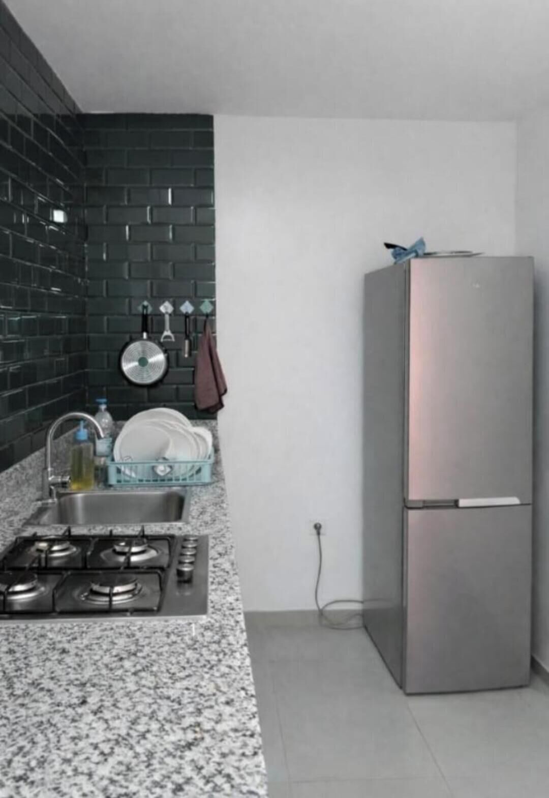 Une cuisine dotée d’un plan de travail en granit, d’appareils électroménagers en acier inoxydable, d’un crédence en carreaux noirs et d’une porte blanche.