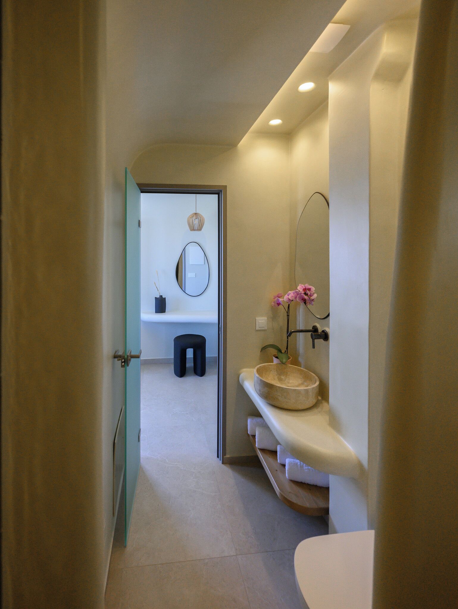 A modern bathroom with a round mirror, a wooden basin, and a small stool.