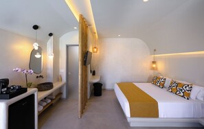 Ein modernes Hotelzimmer mit Bett, Nachttisch, Spiegel und einer kleinen Sitzecke mit Bank und Topfpflanze.