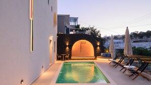 A rooftop pool area with a stone wall, lounge chairs, and umbrellas. - Anemone Luxury Suites (Santorini)