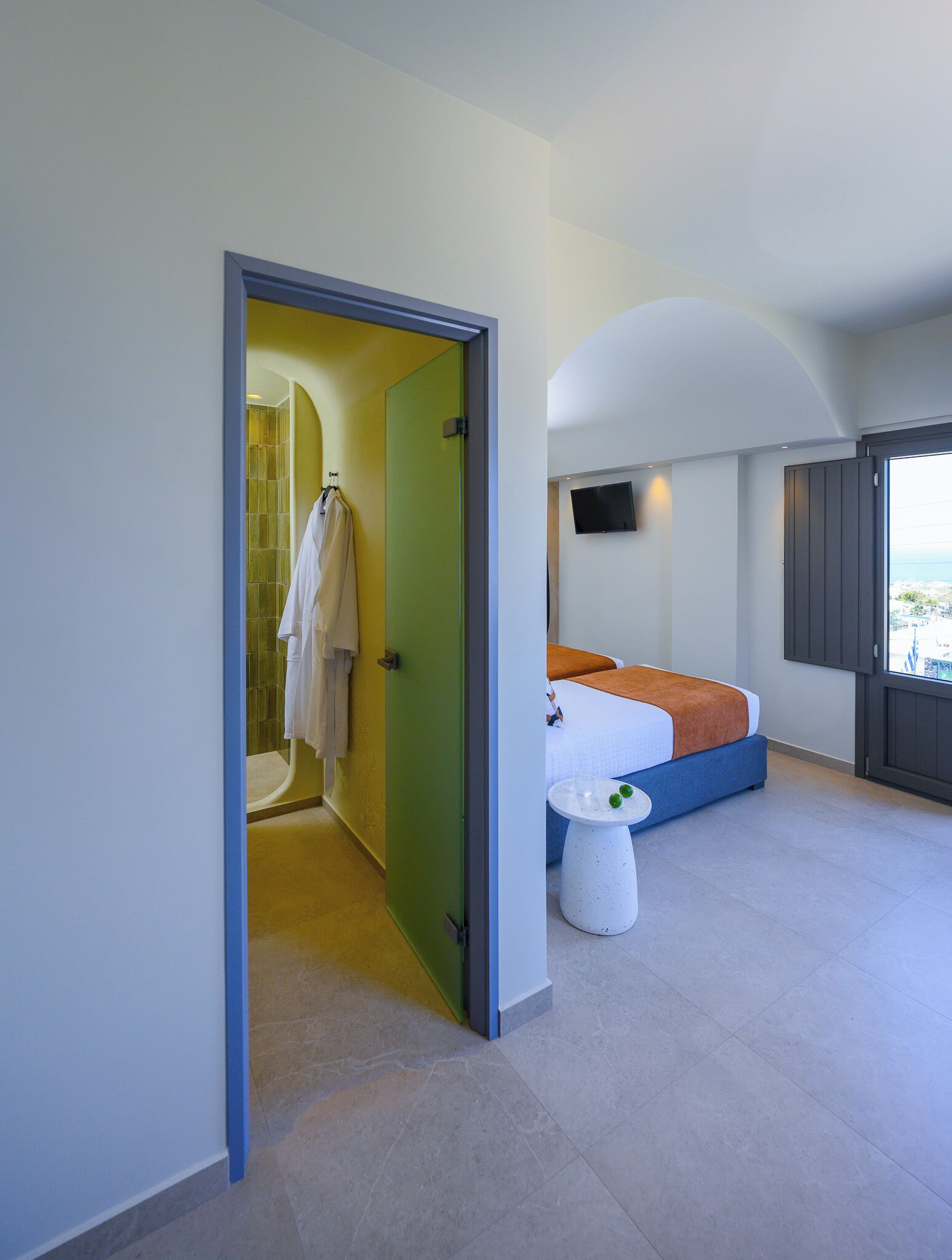 Une chambre d’hôtel moderne, équipée d’un lit, d’une petite table, d’une télévision et offrant une vue sur la mer.